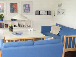A living room with a blue sofa, a white table with a bowl of cookies, a lamp, and a bookshelf. - 5 Person Holiday Home in Aabenraa (Aabenraa)