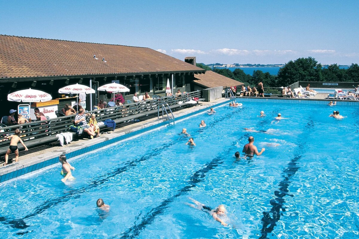 A swimming pool with multiple lanes, spectators, and umbrellas.