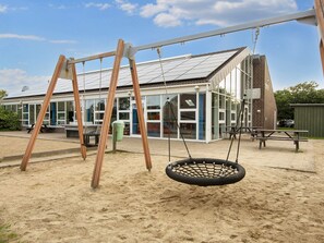Ein Spielplatz mit Schaukeln und einer Reifen-Schaukel, ein Gebäude mit großen Fenstern und ein klarer Himmel.