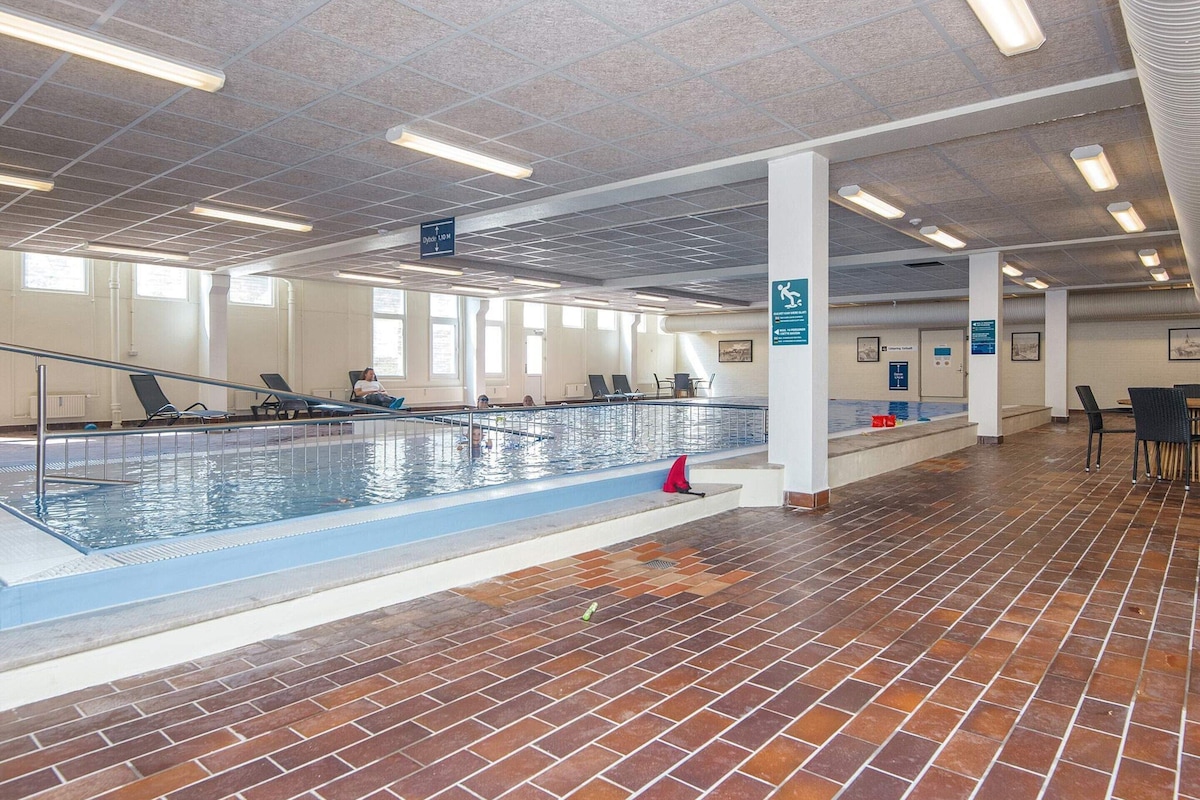 An indoor swimming pool with a tiled floor, clear ceiling with lights, and a few people swimming.