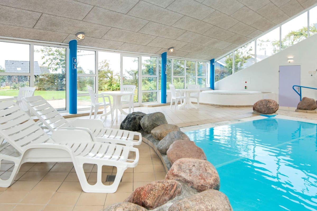 Ein Hallenbad mit weißen Liegestühlen und großen Felsen am Rand.