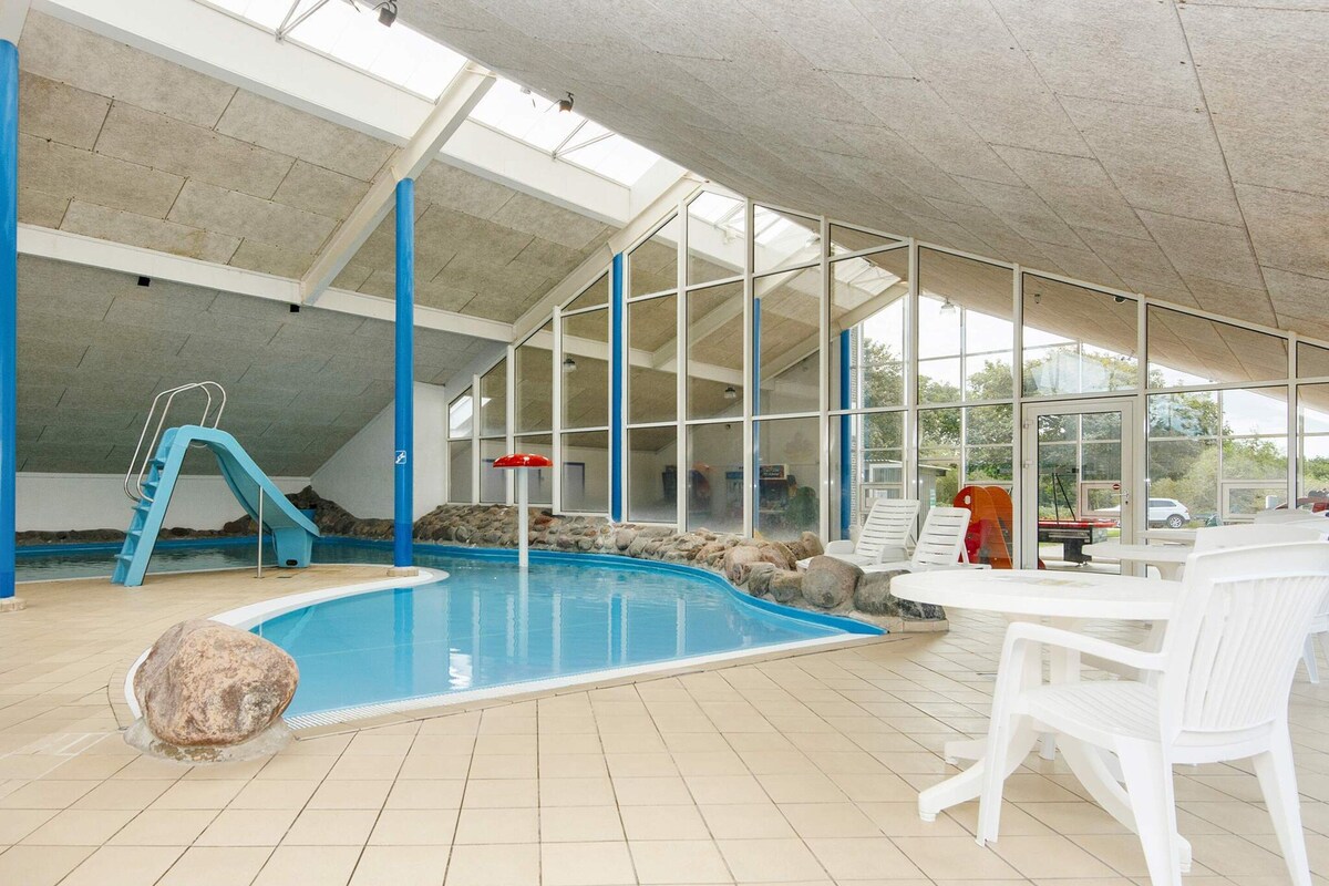Une piscine intérieure avec un toboggan, des chaises longues et une vue sur l’extérieur.