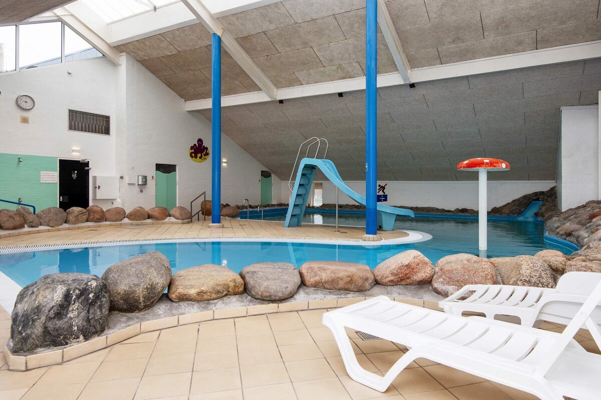An indoor swimming pool with a slide, lounge chairs, and a lifeguard stand.