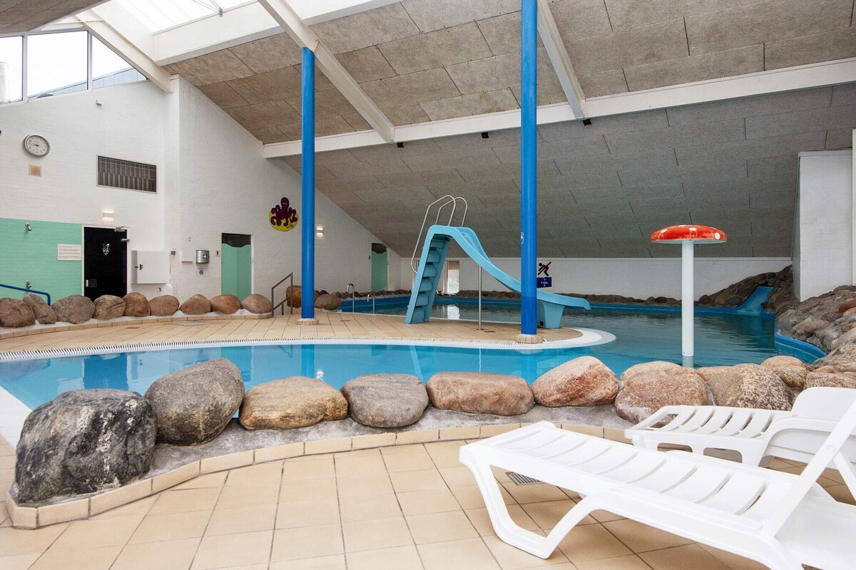 An indoor swimming pool with a slide, lounge chairs, and a lifeguard stand.
