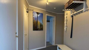 Un couloir avec un plancher en bois, un banc blanc, un tableau représentant une forêt et un luminaire au plafond.