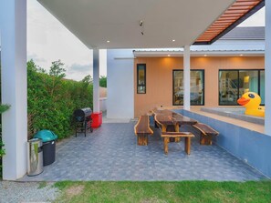 An outdoor patio with a wooden table and benches, a grill, and a trash bin. - Pool&Play - Modern Private Pool Villa in Pattaya (Muang Pattaya)