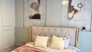 Een moderne slaapkamer met een gestoffeerd hoofdeinde, een groot bed met een roze plaid en decoratieve wandkunst.