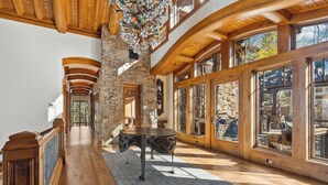 A spacious hallway with wooden floors, stone walls, and large windows. - Lucky Boot Lodge - Incredible Views, Walk to Ski (Edwards)