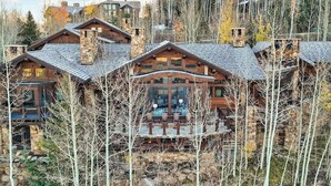A multi-story log cabin with a stone chimney, a deck with outdoor furniture, and a mountainous backdrop. - Lucky Boot Lodge - Incredible Views, Walk to Ski (Edwards)