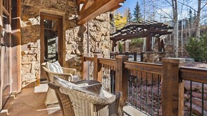 A stone exterior with a wooden balcony, wicker furniture, and a view of trees. - Lucky Boot Lodge - Incredible Views, Walk to Ski (Edwards)