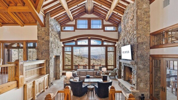 A spacious interior with a stone fireplace, wooden beams, and large windows offering a view of the outdoors. - Lucky Boot Lodge - Incredible Views, Walk to Ski (Edwards)