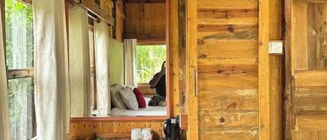 Eine Holzhütte mit einem Bett, einem kleinen Tisch mit Tassen und einer Kaffeemaschine sowie einem Fenster mit Vorhängen.