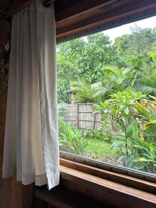 Une fenêtre donnant sur un jardin luxuriant, avec un cadre en bois et un rideau blanc.
