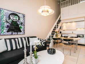 Een moderne woonkamer met een bank, een salontafel met kaarsen en bloemen, een trap en een keukenhoek.