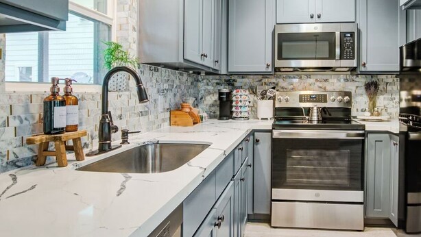 A modern kitchen with grey cabinets, a stainless steel sink, and a built-in microwave.