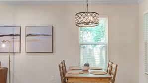 A dining area with a wooden table and chairs, a hanging light fixture, and two framed pictures on the wall.