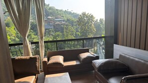 Ein Balkon mit einer Couch, einem kleinen Tisch und Blick auf eine Hügelsiedlung.