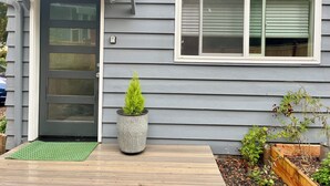 Una casa con facciata grigia, una porta d'ingresso, una finestra con persiane, una pianta in vaso e un patio in legno.