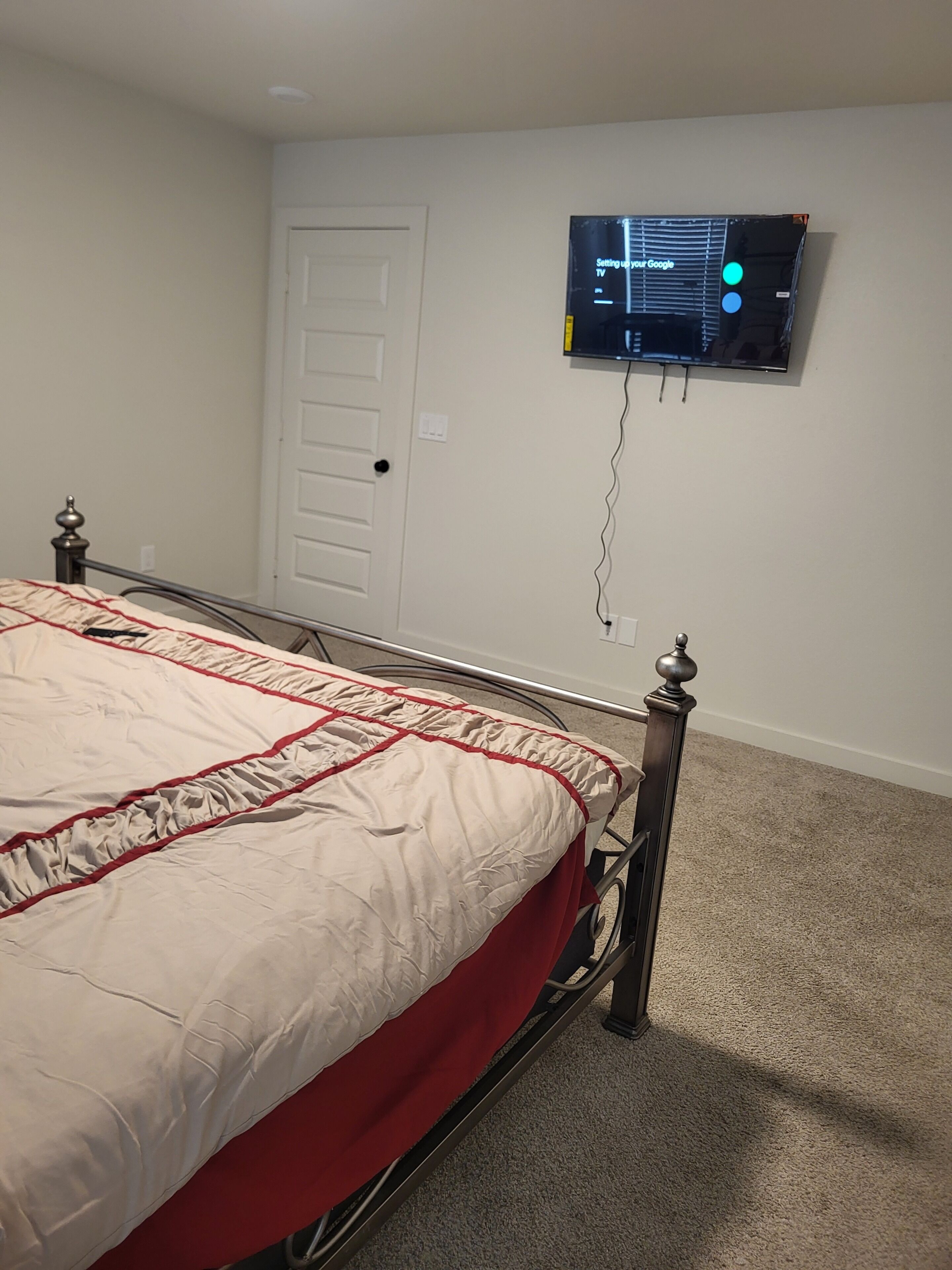 A bedroom with a bed, a television mounted on the wall, and a door.