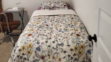 A small, neatly arranged bedroom with a bed, a chair, a desk, and a door.