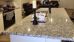 Une cuisine dotée de plans de travail en granit, d’un robinet noir et d’un ventilateur de plafond.