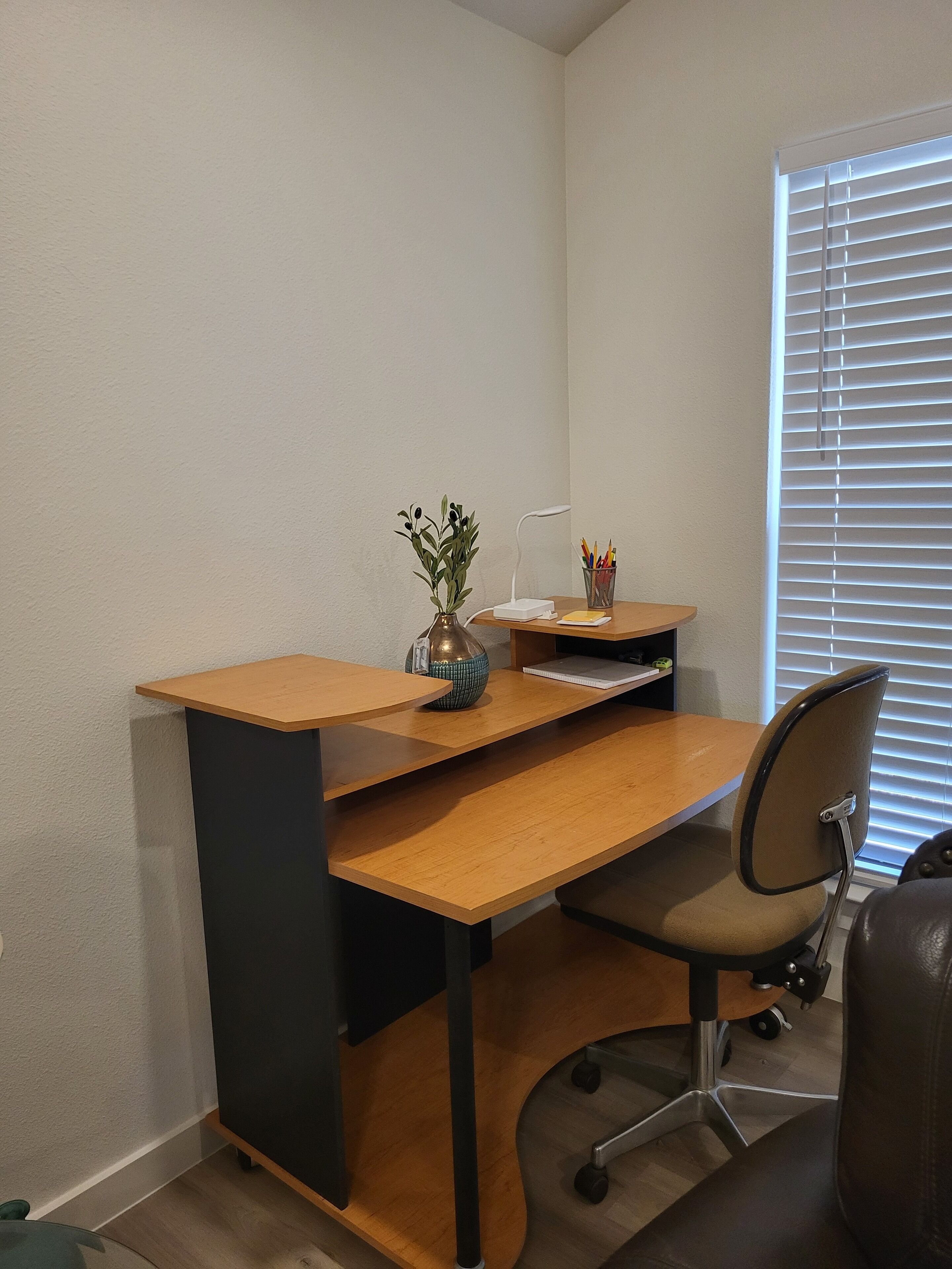 A modern office space with a wooden desk, a chair, a vase with a plant, and a window with blinds.