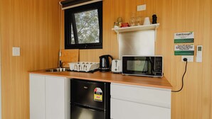 A compact kitchen with a refrigerator, microwave, toaster, and a window with blinds. - Sunset Tiny House at Bluebush Estate X by Tiny Away (Rothbury)