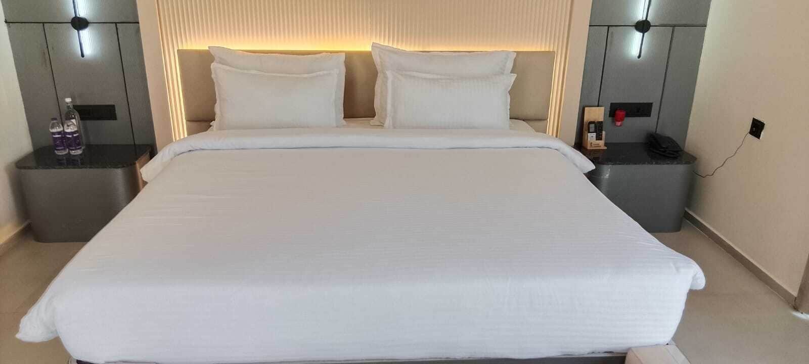 A large bed with white bedding, two bedside tables with lamps, and a wall-mounted light fixture above the bed.