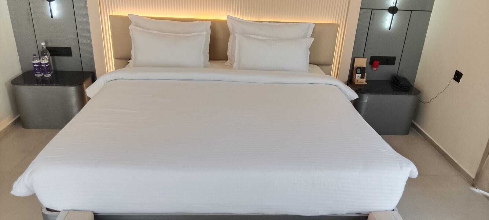 A neatly made bed with white linens, two bedside tables with lamps, and a wall-mounted light fixture.