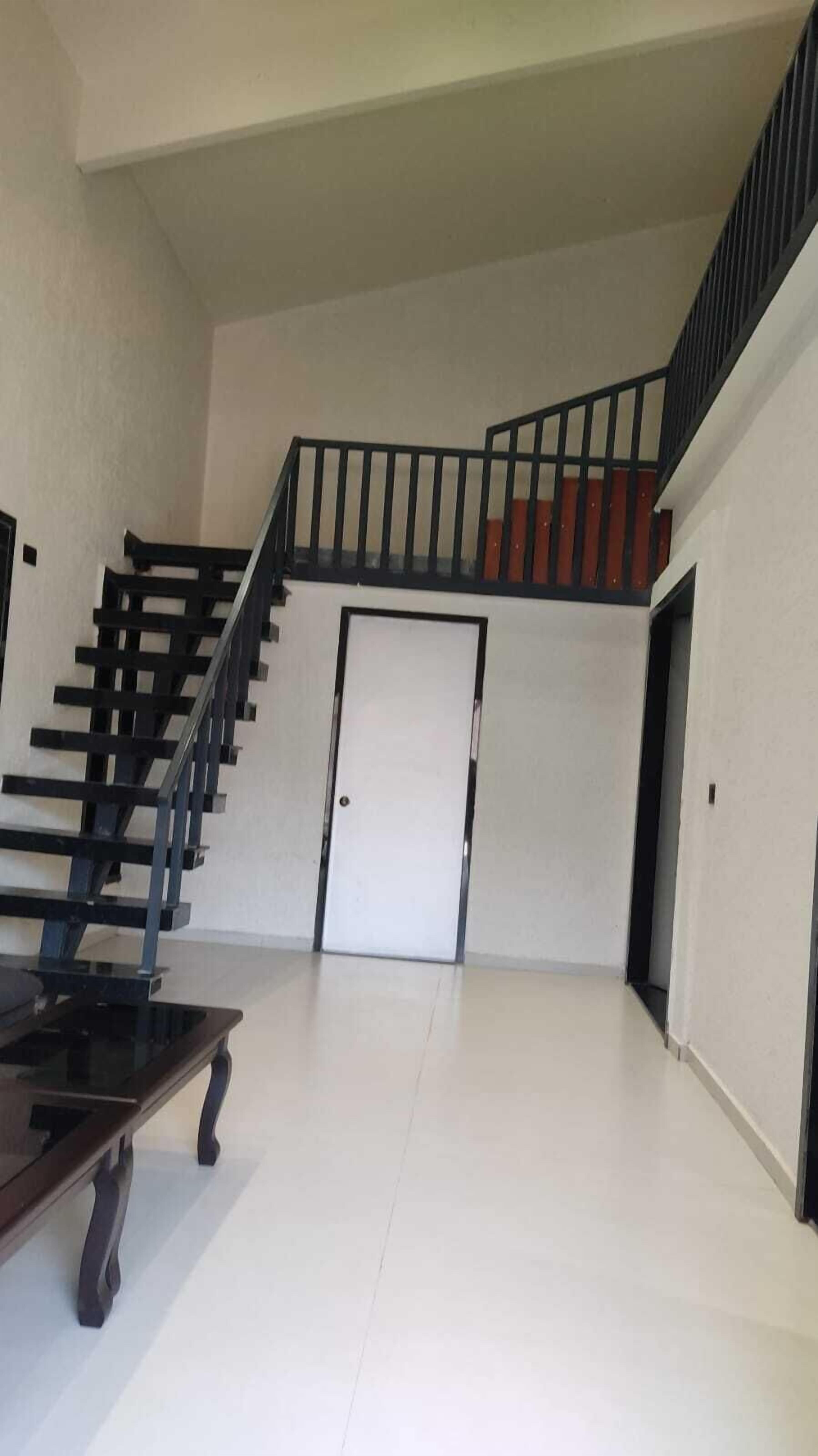 Un interior espacioso con una escalera que conduce a un nivel superior, una puerta y una mesa de madera.