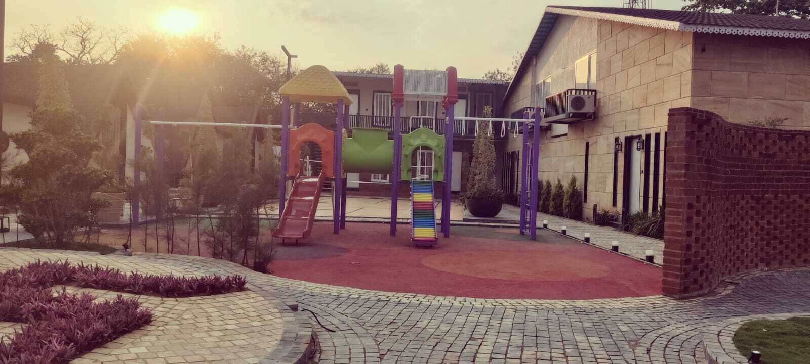 A playground with slides and climbing structures, surrounded by a paved area and a building.
