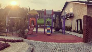 A playground with slides and climbing structures, surrounded by a paved area and a building.