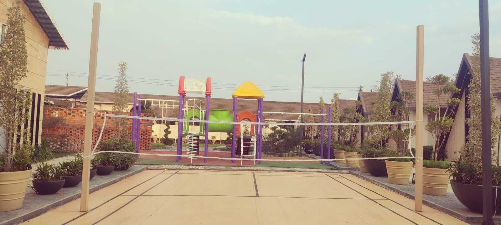 A playground with a climbing structure and a slide, surrounded by potted plants and residential buildings.