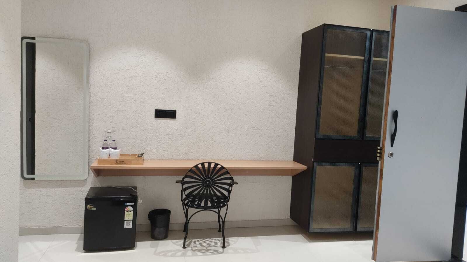 Una kitchenette pequeña con refrigerador, lavamanos y una silla.