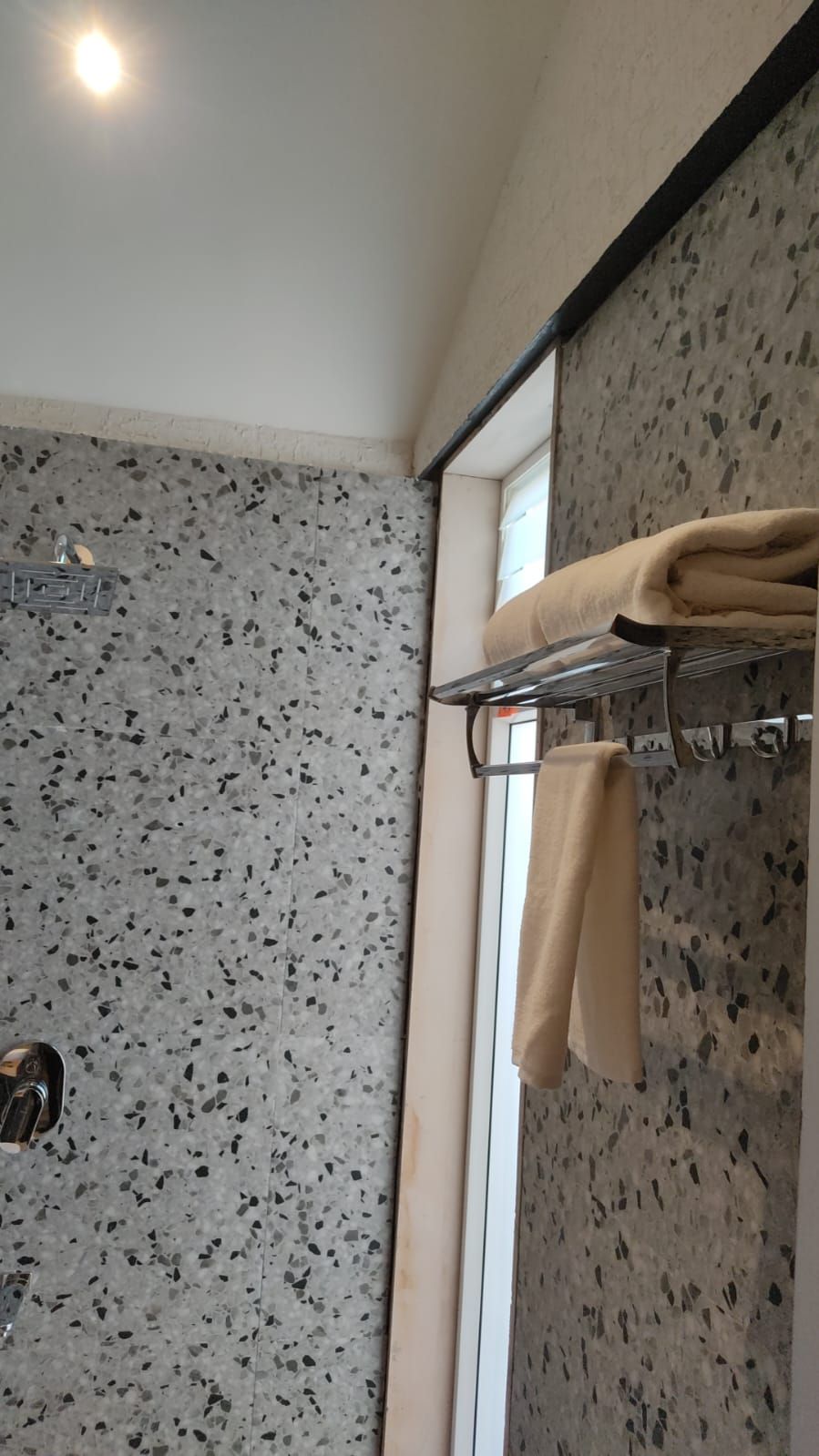 Een badkamer met een puntbestraald vloertje, een handdoekrek met handdoeken, een douchegedeelte en een raam.