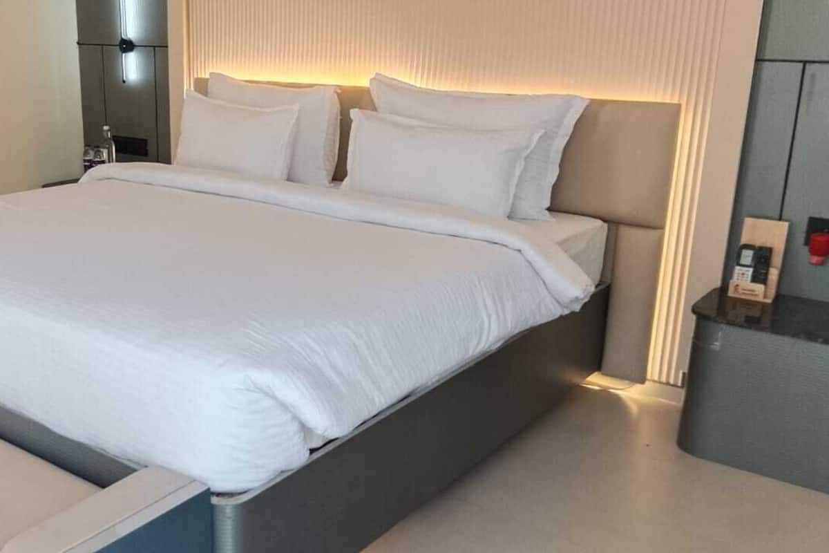 A modern hotel room with a large bed, bedside tables, and a bench at the foot of the bed.