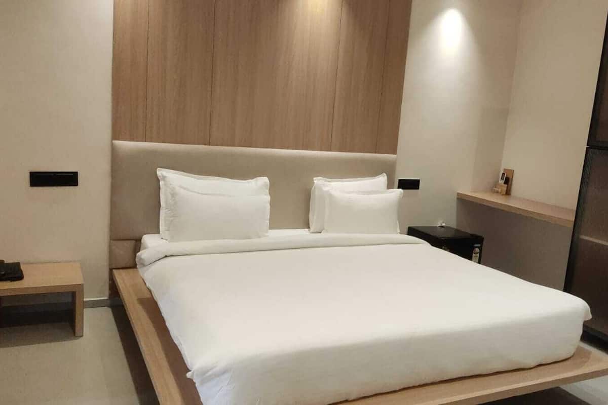 A modern hotel room with a large bed, a wooden headboard, a bedside table, and a wardrobe.