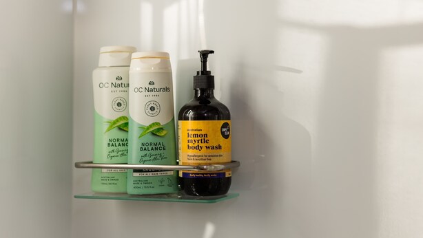 Une étagère de salle de bain avec trois flacons de produits pour les soins capillaires et un gel douche.
