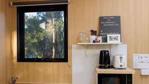 A modern kitchen with a sink, a coffee maker, a toaster, and a microwave. There's a window with a view of trees and a welcome sign.