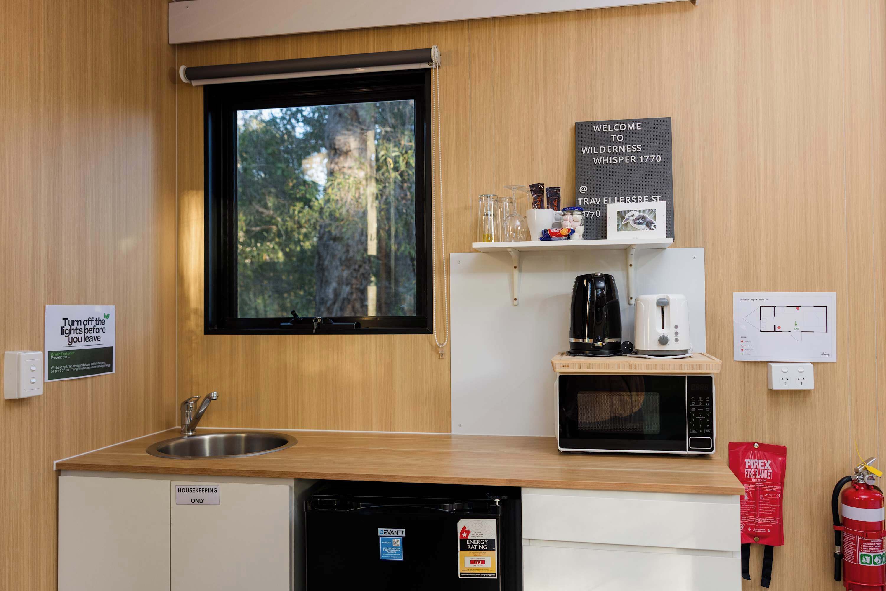 A compact kitchen with a sink, a microwave, a coffee maker, and a fire extinguisher.