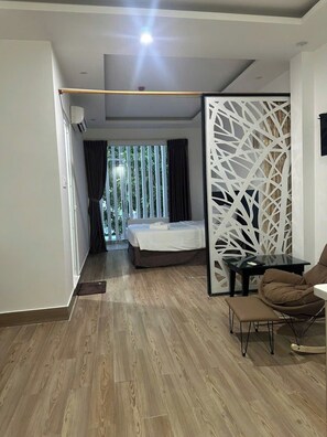 A modern hotel room with a bed, a seating area with a table and chairs, and a view of greenery through the window. - Full House Hotel And Apartment (Da Nang)