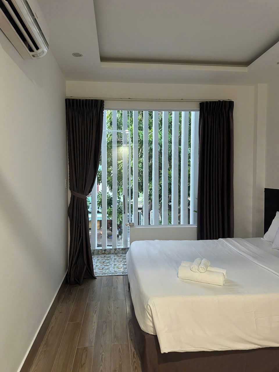 Quarto de hotel com uma cama grande, vista através de uma porta deslizante para uma área externa, e um ar condicionado na parede.