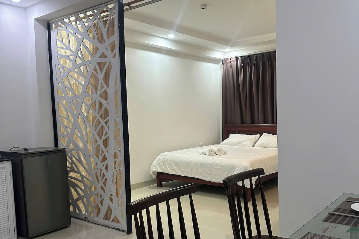 Une chambre d’hôtel comprenant un lit, une table à manger en verre avec des chaises, un petit réfrigérateur et un élément de séparation décoratif.