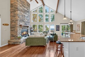 Un salón espacioso con chimenea de piedra, ventanas amplias e isla de cocina.