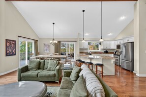 A spacious living room with a green sofa, a dining area with a table and chairs, and a kitchen with stainless steel appliances. - Mountain retreat w/deck, game room & dog-friendly (Hedgesville)