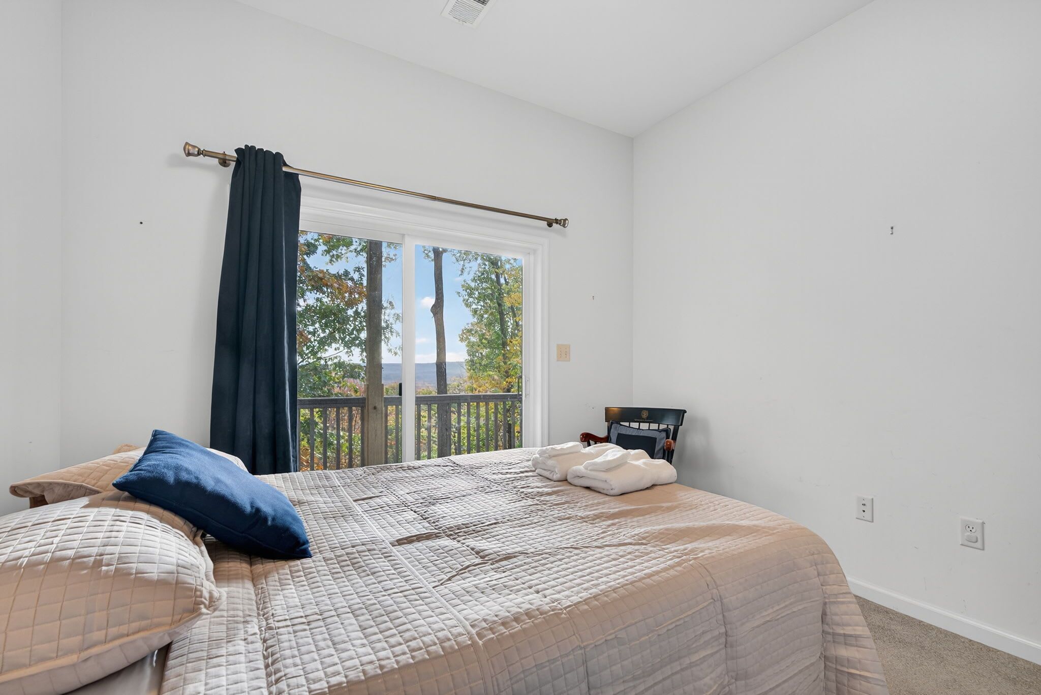 A bedroom with a large window, a bed with a quilted bedspread, two pillows, and a headboard with a clock.