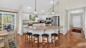 A modern kitchen with white cabinets, a large island with bar stools, and pendant lighting. - Mountain retreat w/deck, game room & dog-friendly (Hedgesville)