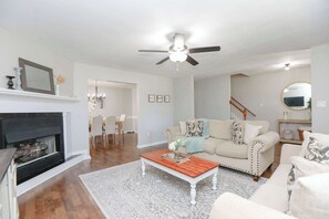 A living room with a fireplace, a ceiling fan, a coffee table, and a sofa. - Sojourn Delightful Family Home Sleeps 6 (Norfolk)