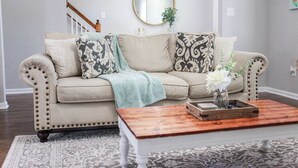 A living room with a beige sofa, patterned cushions, a wooden coffee table, and a mirror on the wall. - Sojourn Delightful Family Home Sleeps 6 (Norfolk)