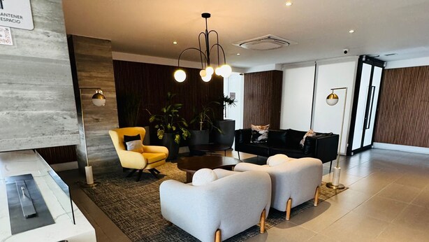 A modern living room with a sofa set, a yellow armchair, and a black sofa. There are potted plants, a coffee table, and a rug. - Alameda Apartment (Tijuana)